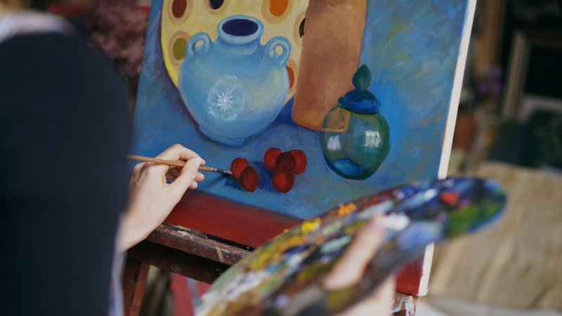 Artist painting a still life with blue vase and fruit.