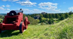 Red cannon on grassy hill overlooking historic buildings