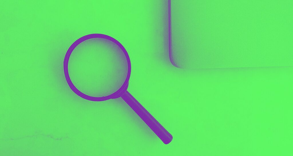 Magnifying glass sits near a laptop on a table.