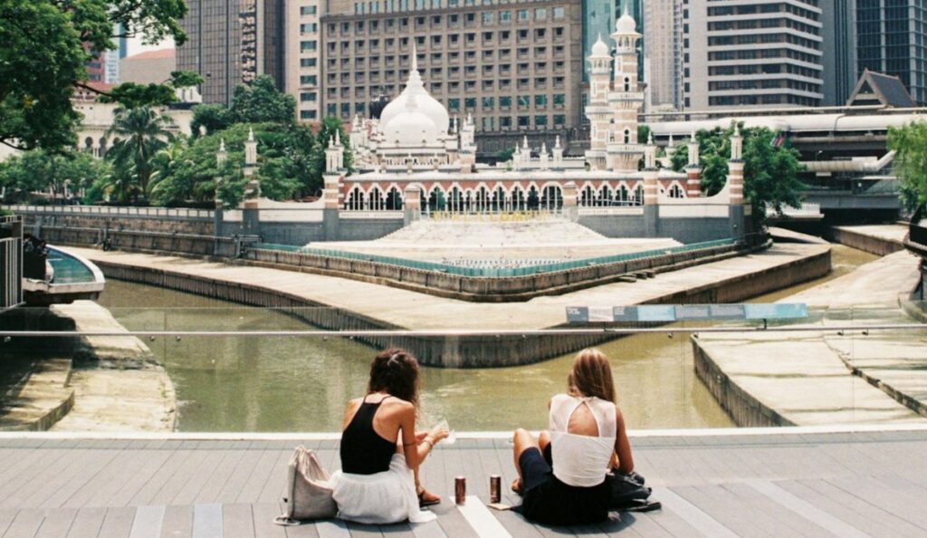 two women sitting on concrete pavement facing on mountain during daytime