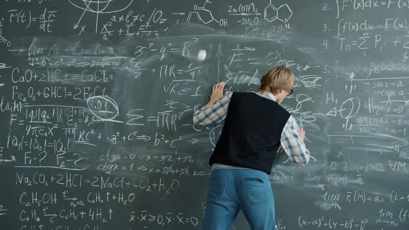 Student writing complex equations on a chalkboard