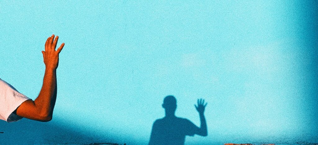 person waving reflecting shadow on teal wall paint