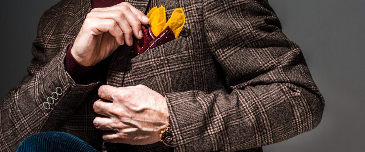 cropped view of fashionable mature man sitting on chair and touching handkerchief on grey cropped view of fashionable mature man sitting on chair and touching handkerchief on grey