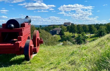 Red cannon on grassy hill overlooking historic buildings