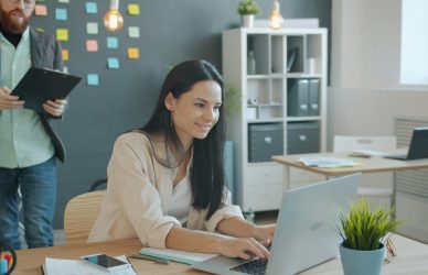 Woman working on laptop with man behind her